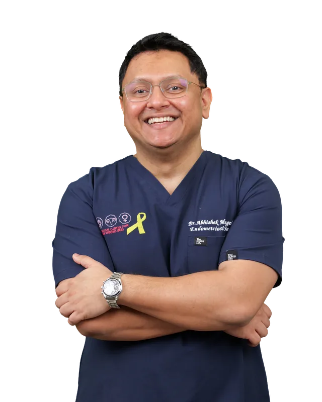 Dr. Abhishek Mangeshikar in navy scrubs, arms crossed, smiling.