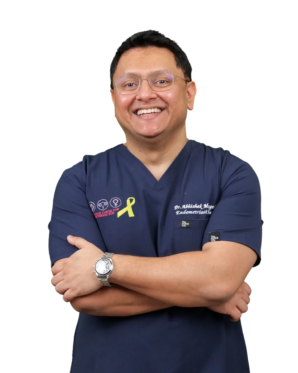 Dr. Abhishek Mangeshikar in navy scrubs with the yellow endometriosis awareness ribbon, arms crossed, smiling.